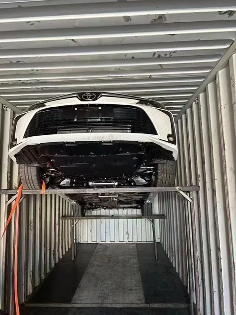 White Toyota positioned on a steel loading rack inside a container