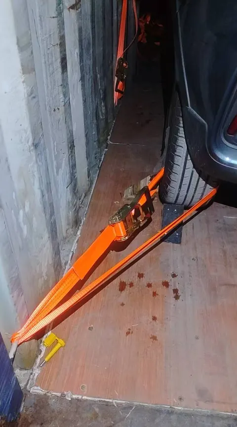Close-up of orange ratchet straps beside a vehicle wheel inside a container